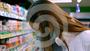 A girl in a medical mask examines food products in a supermarket. Lockdown