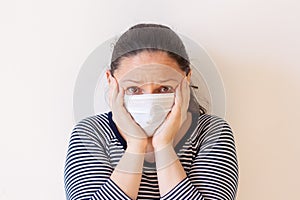 A girl in a medical mask in fear presses her hands to her head.