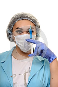 A girl in a medical mask, gloves and a robe with a syringe in his hands on a white background. Beautician, beauty specialist.