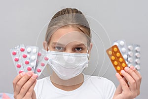A girl with a medical mask on her face holds blisters with medicines