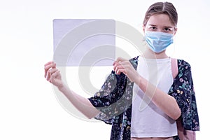 Girl in a medical mask holds a white sheet of paper in her hands