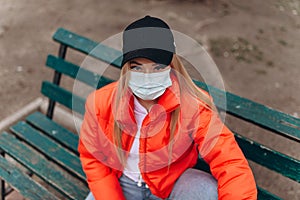 Girl in medical mask protecting, against viruses while sitting on a bench on the street