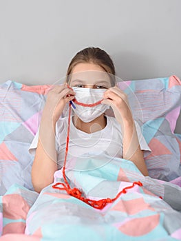 A girl in a medical mask in quarantine knits and made a smile out of thread on the mask