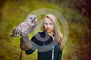 Girl in medieval dress is holding an owl on her arm
