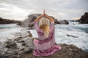 Girl meditates sitting on the rocks looking at the ocean and she does yoga, spirituality concept