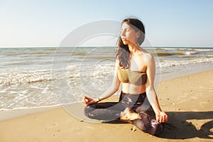 Girl meditating in lotus yoga on coast of sea on the beach. Young beautiful healthy woman making meditation on the beach