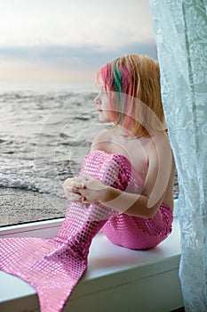 Girl-mermaid sits on the window