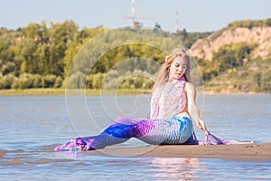 Girl with a mermaid tail on the river bank. Mystical and fairytale heroine. A sensation on vacation
