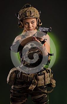 The girl in military airsoft clothes poses with a gun in her hands on a dark background