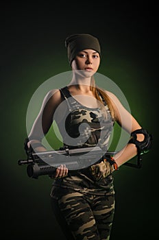 The girl in military overalls airsoft posing with a gun in his hands on a dark background in the haze