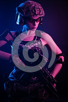 The girl in military overalls airsoft posing with a gun in his hands on a dark background in the haze in neon light