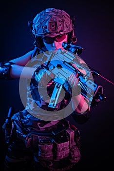 The girl in military overalls airsoft posing with a gun in his hands on a dark background in the haze in neon light