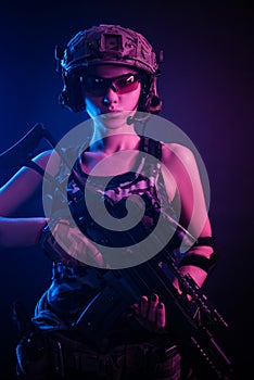 The girl in military overalls airsoft posing with a gun in his hands on a dark background in the haze in neon light