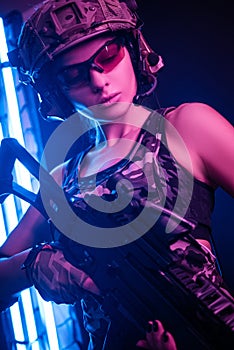 The girl in military overalls airsoft posing with a gun in his hands on a dark background in the haze in neon light