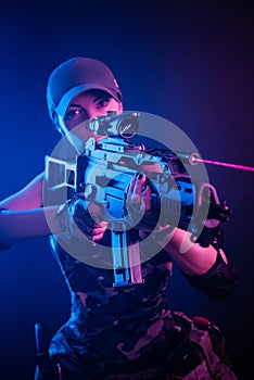 The girl in military overalls airsoft posing with a gun in his hands on a dark background in the haze in neon light