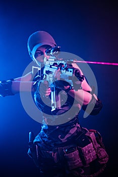 The girl in military overalls airsoft posing with a gun in his hands on a dark background in the haze in neon light