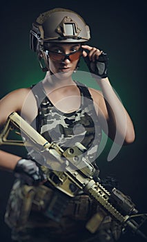The girl in military special clothes posing with a gun in his hands on a dark background in the haze
