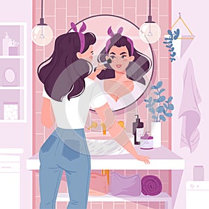 Young woman standing in front of a mirror applies makeup in bathroom. photo