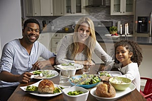 Girl and mixed race parents dine in their kitchen, to camera