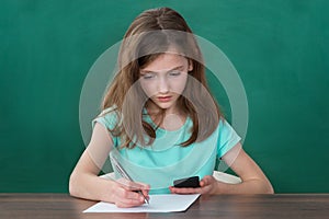 Girl With Mobile Phone Writing On Paper