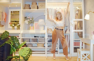 Girl model posing against the backdrop of a wardrobe with clothes. Woman in trousers and white top showing her room  gardirop