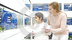 Girl with mother choosing aquarium fish while shopping in pet store