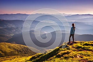 Girl on mountain peak with green grass looking in mountains