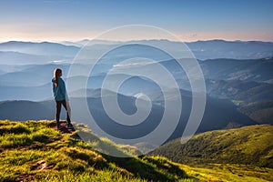 Girl on mountain peak looking at beautiful mountains at sunset