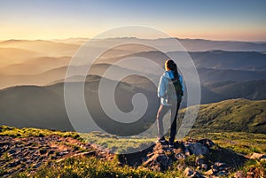 Girl on mountain peak looking at beautiful mountains at sunset