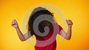 Girl moves to the rhythm of music. Woamn with curly hair dancing on yellow background. Female having fun. She smiling