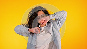 Girl moves to the rhythm of music. Woamn with curly hair dancing on yellow background. Female having fun. She smiling