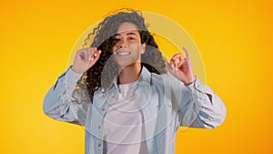 Girl moves to the rhythm of music. Woamn with curly hair dancing on yellow background. Female having fun. She smiling