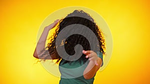 Girl moves to the rhythm of music. Woamn with curly hair dancing on yellow background. Female having fun. She smiling