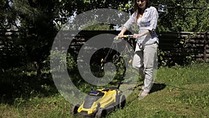 The girl is mowing an uneven lawn with yellow lawnmower barefoot