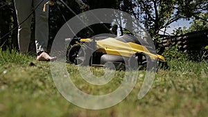 The girl is mowing an uneven lawn with yellow lawnmower barefoot