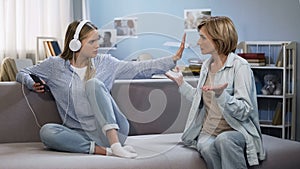Girl in music headphones showing stop gesture to shouting mother, generation gap