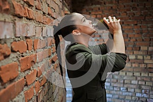 Girl near the brick wall in military style.