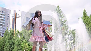 A girl near a fountain in the park after shopping with bags in hand. slow motion.