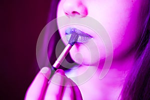 Girl in neon light with blue lipsteak on her lips.