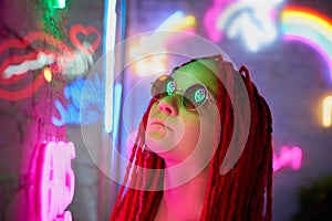 Girl in neon lights, beautiful woman in sunglasses, with pink hair, with dreadlocks pigtails, bright and stylish in glow of neon