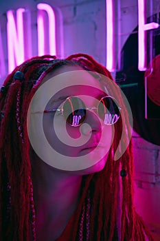 Girl in neon lights, beautiful woman in sunglasses, with pink hair, with dreadlocks pigtails, bright and stylish in glow of neon