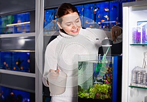 Girl with net and water container is going to catch juvenile fish from aquarium