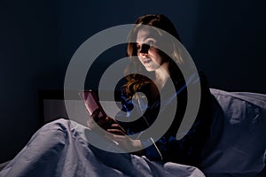 Girl at night in the bed sitting in internet before going to sleep.