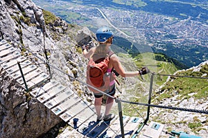 Girl on Nordkette via ferrata wooden bridge looks down over Innsbruck city, Austria. Klettersteig, summer, adventure, active.