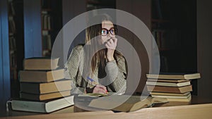 Girl noting compendium from books at a desk and gazing into it in half-light