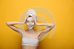 Girl with nourishing facial mask and towel on head looking away on yellow background