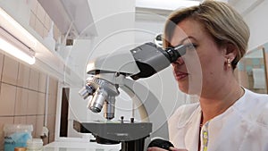 The girl nurse carefully examines the bacteria through a microscope.