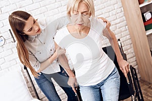 Girl is nursing elderly woman at home. Girl is helping woman to get into wheelchair.