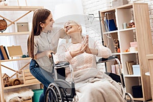 Girl is nursing elderly woman at home. Girl is riding woman in wheelchair. Woman is enjoying herself.