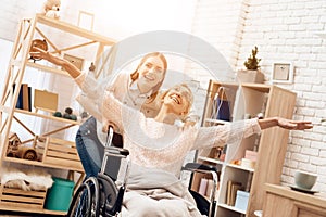 Girl is nursing elderly woman at home. Girl is riding woman in wheelchair. Woman feels like flying.